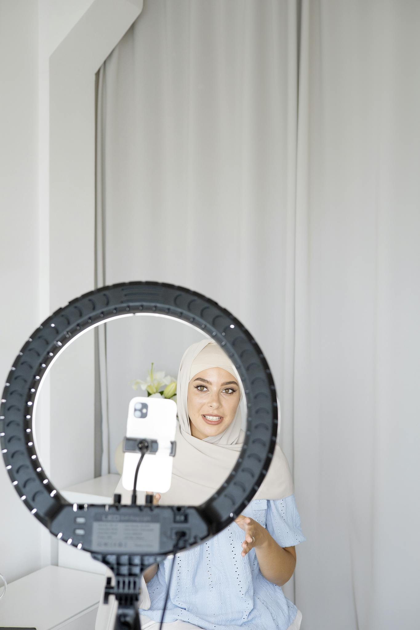 Woman in hijab recording a vlog with a smartphone and ring light.