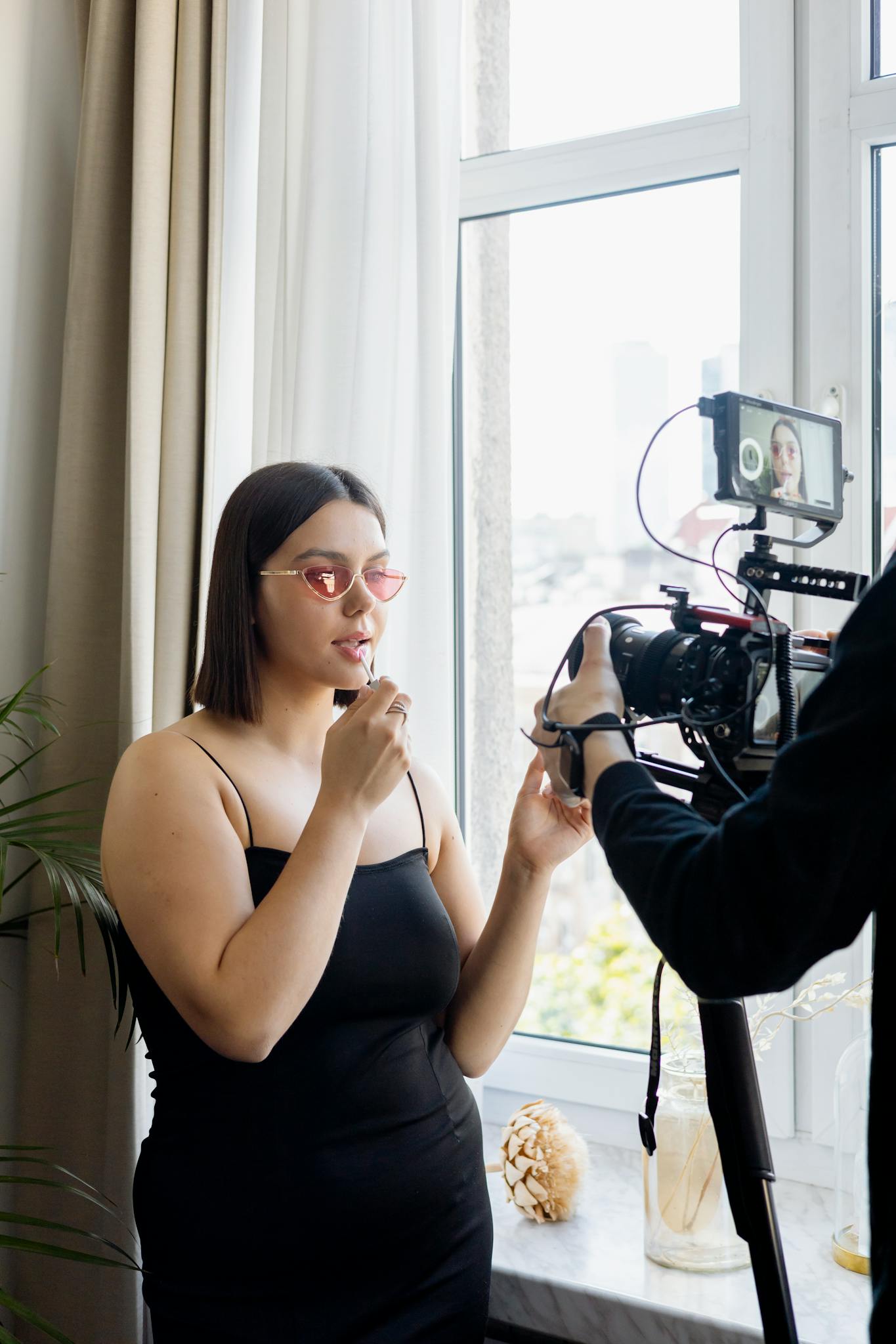 Young woman films a makeup tutorial at home with a professional DSLR camera setup.